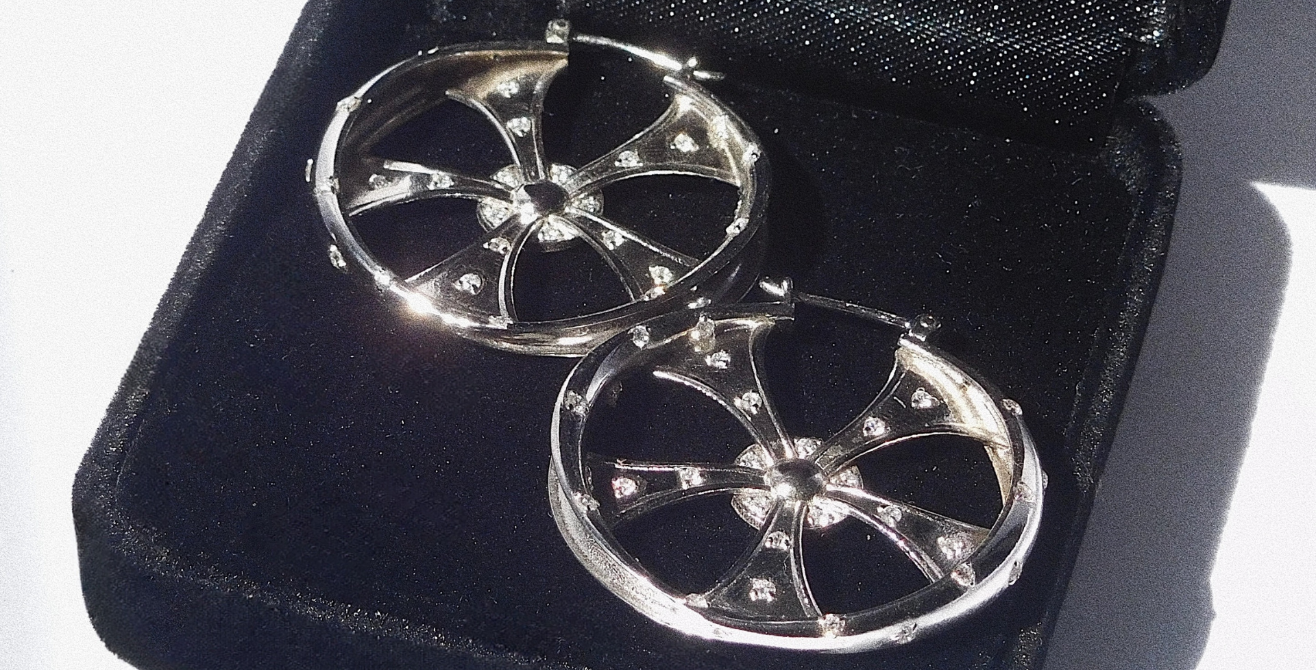 Pair of silver earrings with intricate design on a black stand.