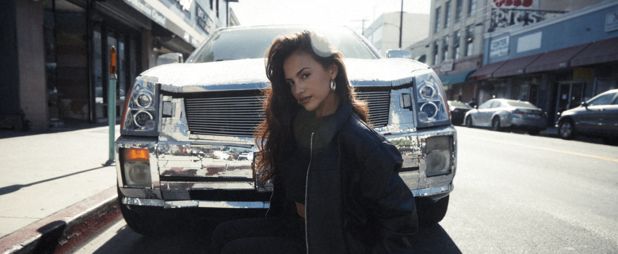 Woman standing in front of a shiny white SUV on a city street